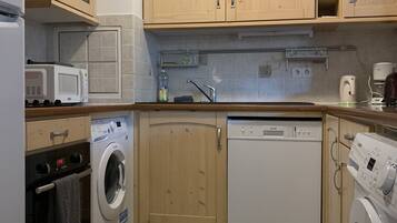A compact kitchen with wooden cabinets, a washing machine, a dishwasher, and a microwave.