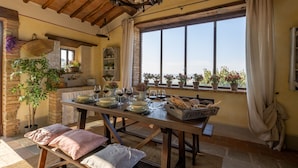 Un coin repas rustique avec une table en bois dressée pour le repas, entouré de plantes en pot et offrant une vue sur la campagne.