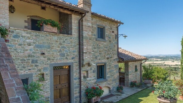 Une maison en pierre avec une porte en bois, des plantes en pot et une vue sur la campagne.