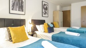 Ein Hotelzimmer mit zwei Betten, jeweils mit blauer Bettdecke und mehreren Kissen. Es gibt einen Schrank und ein gerahmtes Bild an der Wand.