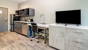 Une cuisine moderne équipée d’un four à micro-ondes, d’un réfrigérateur et d’un évier. On y trouve un bureau avec une chaise et un téléviseur posé sur un meuble.