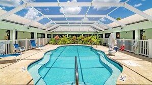 Une piscine intérieure à l’eau d’un bleu cristallin, entourée de chaises longues et d’un espace abrité surmonté d’un toit blanc.