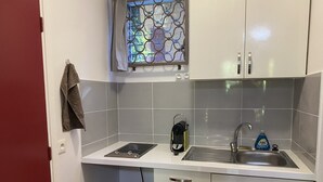 Cocina compacta con estufa a gas integrada, un lavamanos y un ventanal con celosía de metal decorativa.