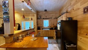 A wooden cabin interior with a kitchen area, wooden bar stools, and a refrigerator. - Rangeley Getaway (Dallas Plantation)