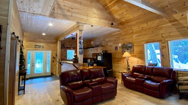A spacious living area with wooden floors and a high ceiling, featuring two leather sofas and a kitchen area in the background. - Rangeley Getaway (Dallas Plantation)