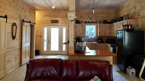 A cabin interior with a living area, kitchen, and a door leading to another room. - Rangeley Getaway (Dallas Plantation)