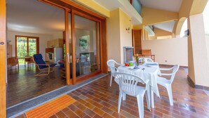 Un vaste espace patio aménagé avec une table et des chaises, une porte-fenêtre coulissante donnant sur une pièce baignée de lumière et une vue sur l’extérieur.