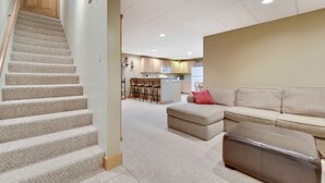 A spacious living area with a staircase, a sofa set, a coffee table, and a kitchen in the background.