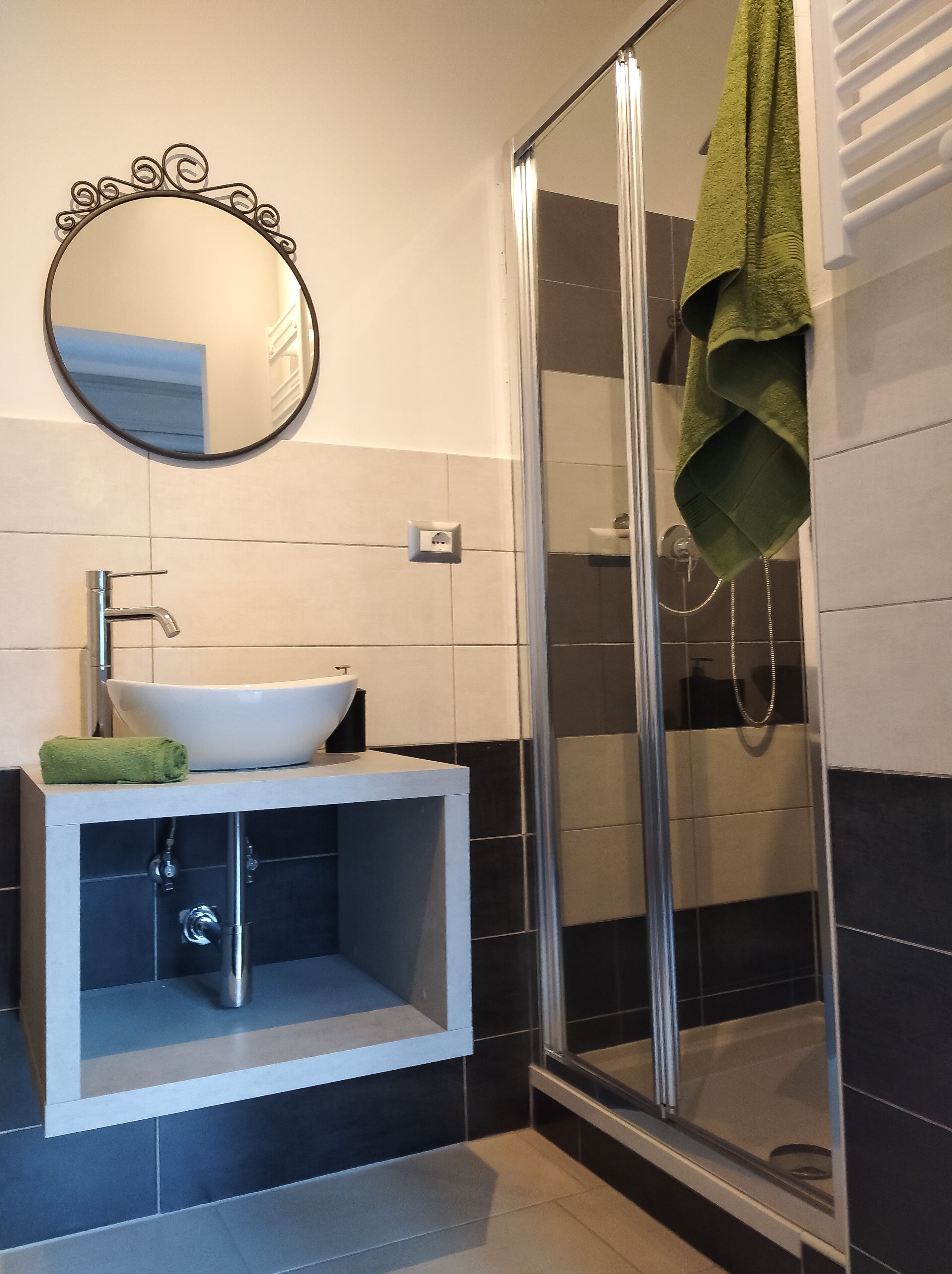 A bathroom with a white sink, a mirror with a decorative frame, a green towel, and a glass shower enclosure.