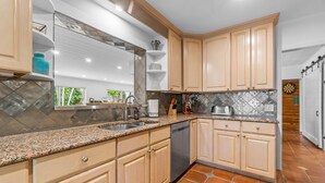 A kitchen with light wood cabinets, granite countertops, and a dishwasher.