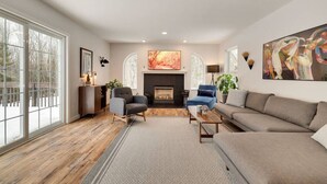 Ein großzügiges Wohnzimmer mit Kamin, großen Fenstern und modernen Möbeln.
