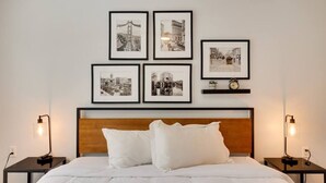 Ein Hotelzimmer mit einem Bett, weißer Bettwäsche, einem hölzernen Kopfteil und vier schwarz-weißen Fotografien an der Wand.