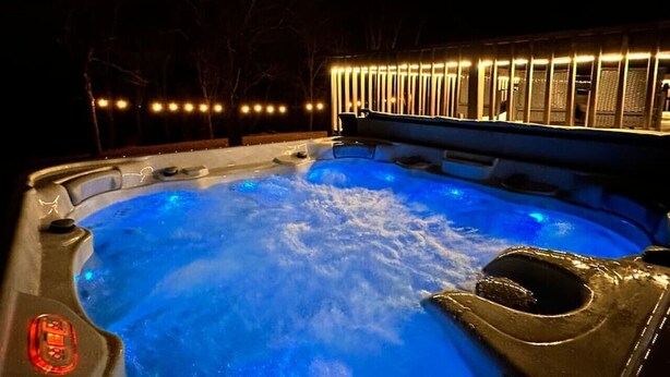 Ein Whirlpool mit blauem Licht, umgeben von einer Holzterrasse und einem mit Lichtern versehenen Zaun.