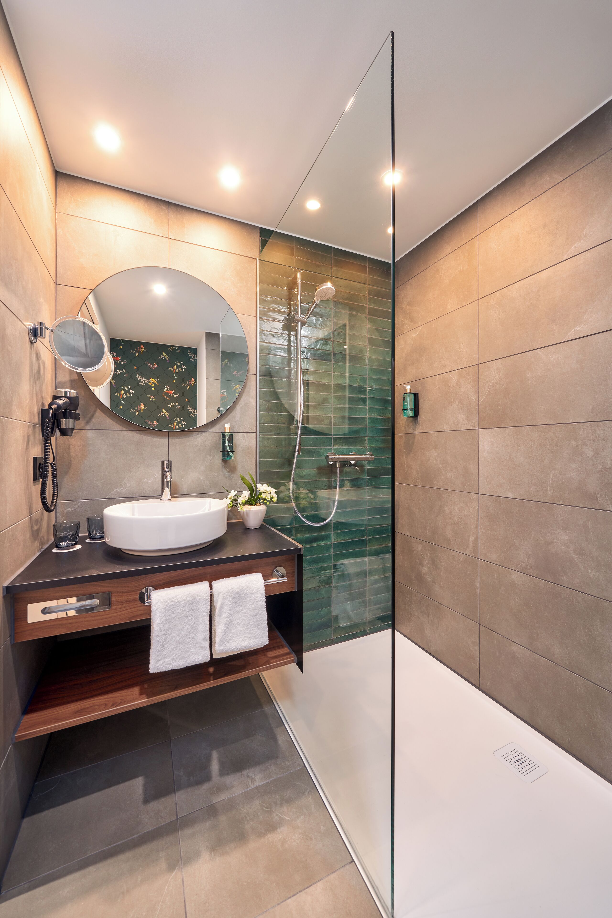 A modern bathroom with a round mirror, a white sink, and a glass-enclosed shower.
