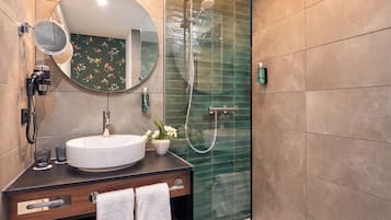 A modern bathroom with a round mirror, a white sink, and a glass-enclosed shower.