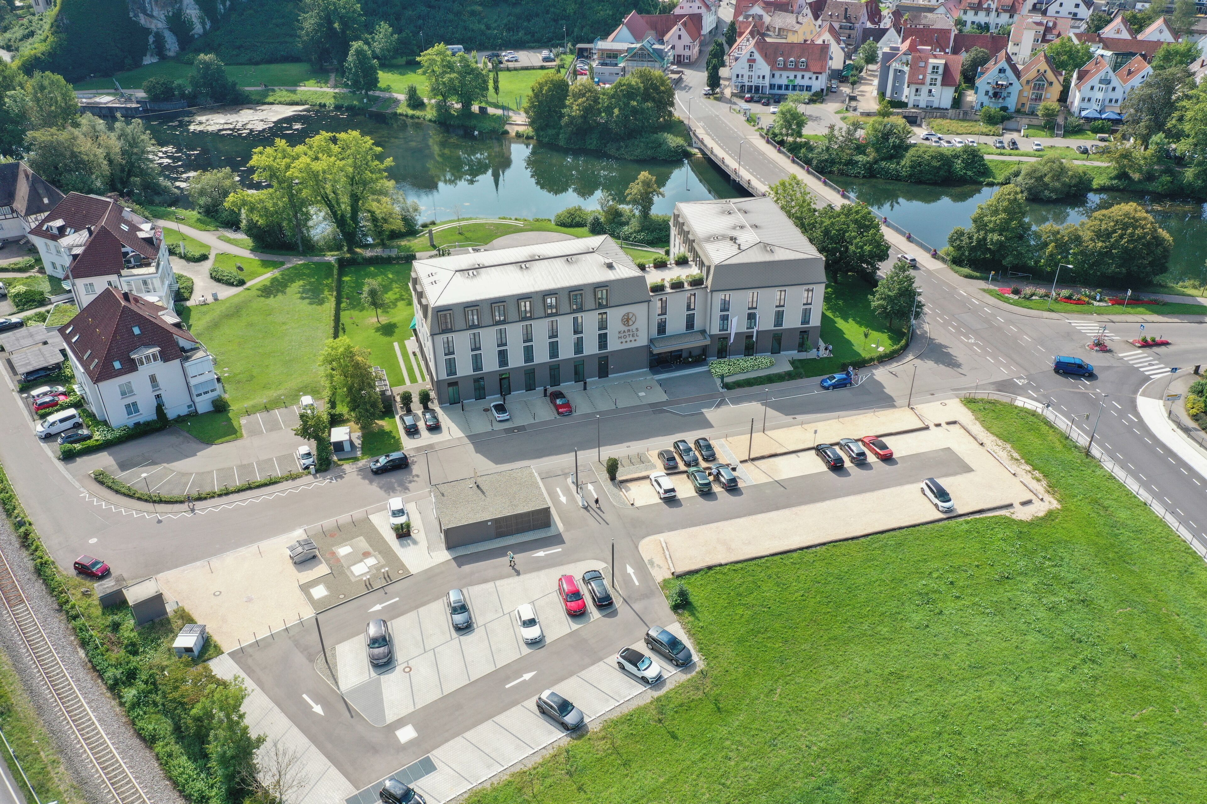 An aerial view of a hotel with a parking lot, a river, and surrounding greenery.