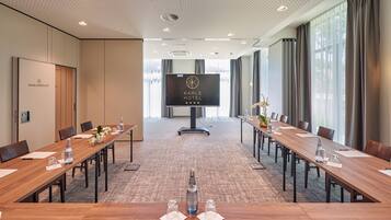 A conference room with a long table, chairs, a television screen, and a logo for Karls Hotel.