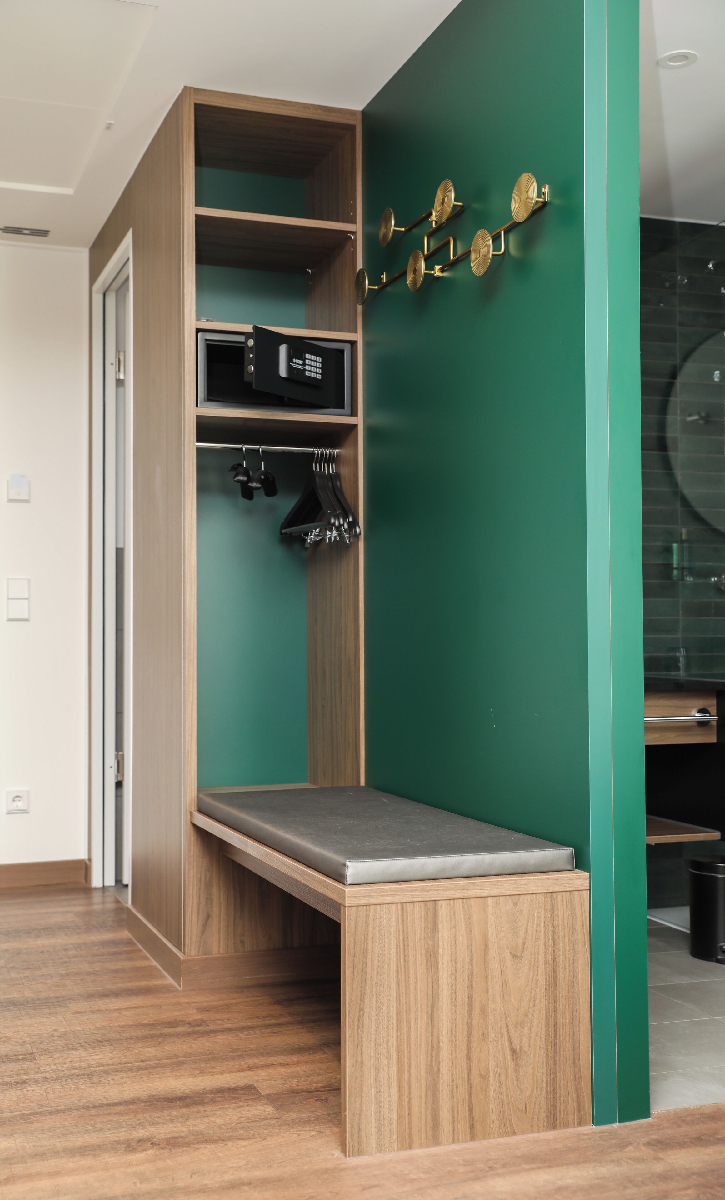 Habitació compacta amb una cadira-llit integrada, una petita estant amb un objecte negre i una paret verda decorativa.