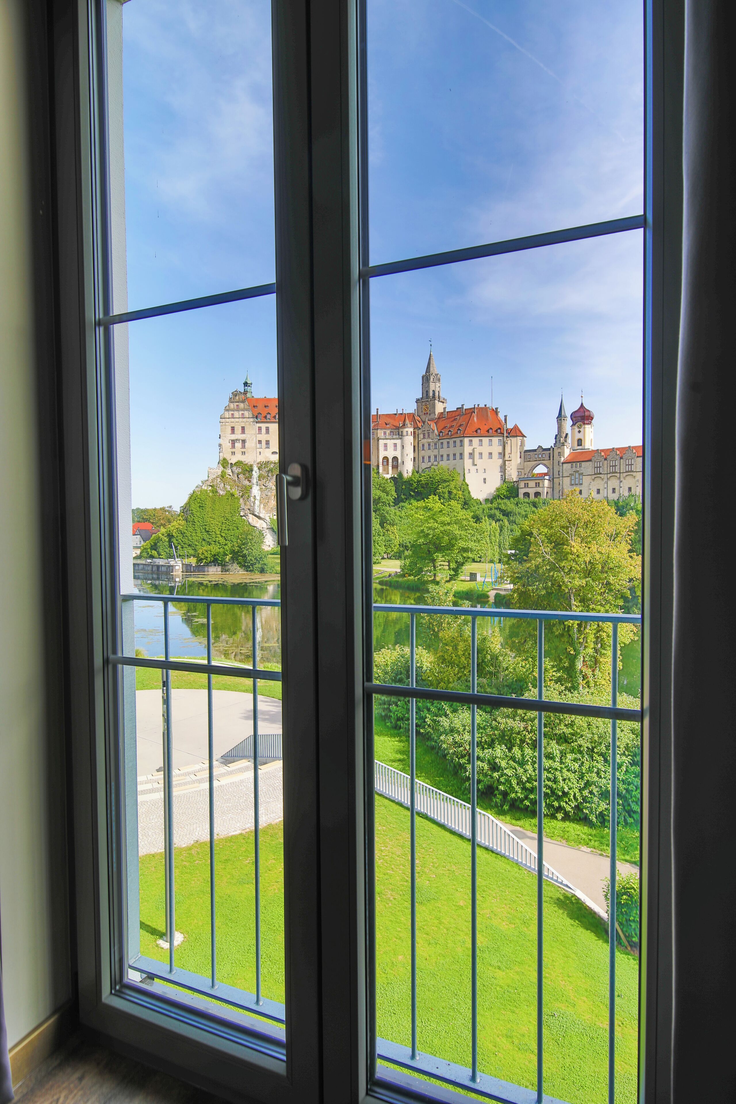 A view through a window with a balcony, overlooking a castle and a river.