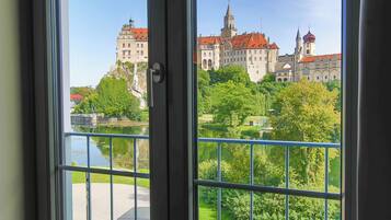 A view through a window with a balcony, overlooking a castle and a river.
