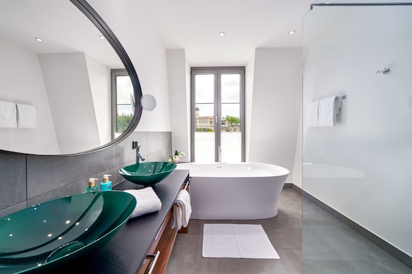 Un baño moderno con una bañera independiente, un espejo grande y un lavabo de vidrio verde.