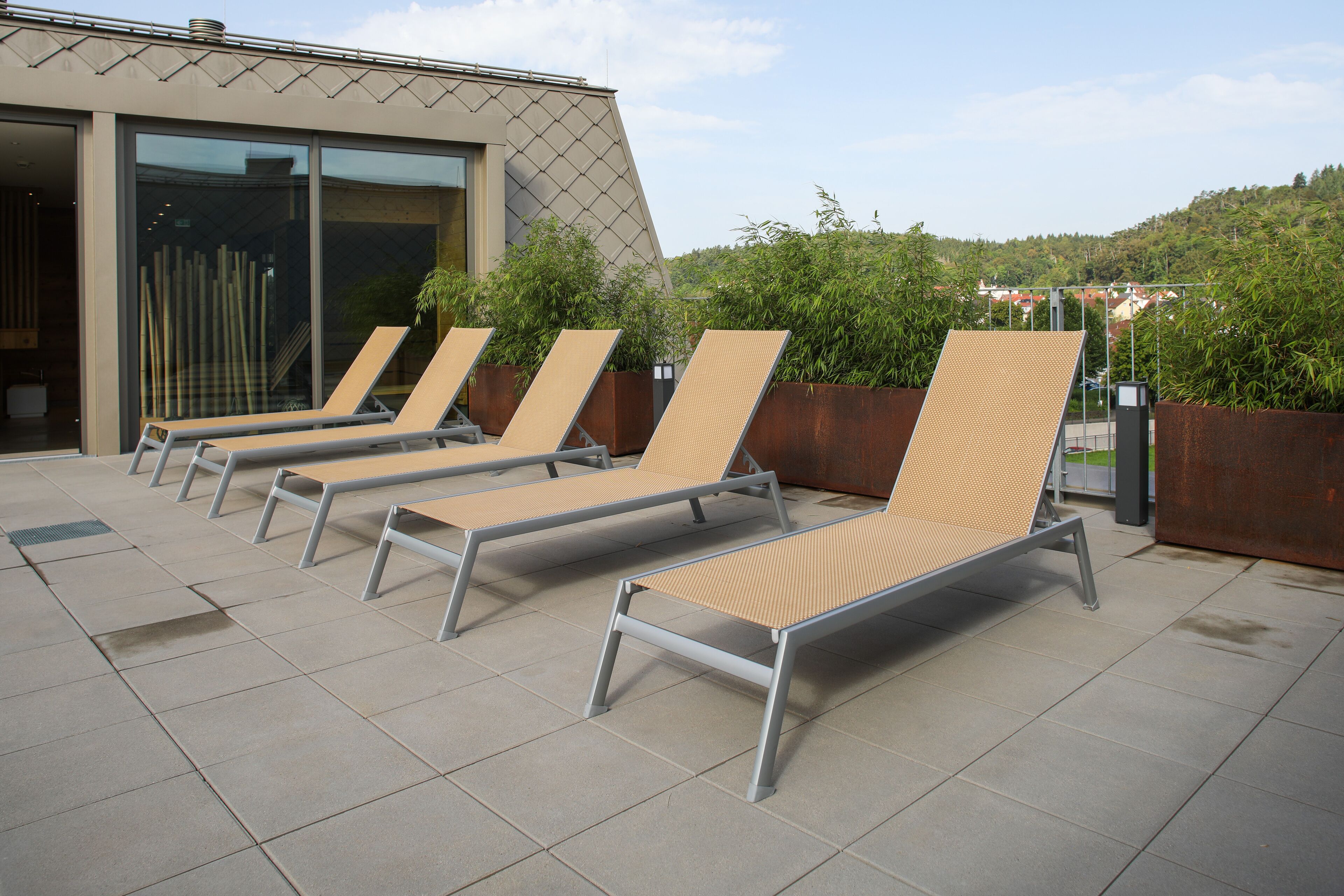 A row of sun loungers on a tiled patio with a modern building in the background.