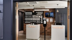 A hotel reception area with a check-in counter, a 'CARDIFF' sign, and a 'WELCOME' sign. - easyHotel Cardiff (Cardiff)