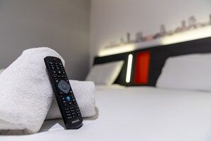 A remote control on a white towel on a bed with a modern headboard and a cityscape view.