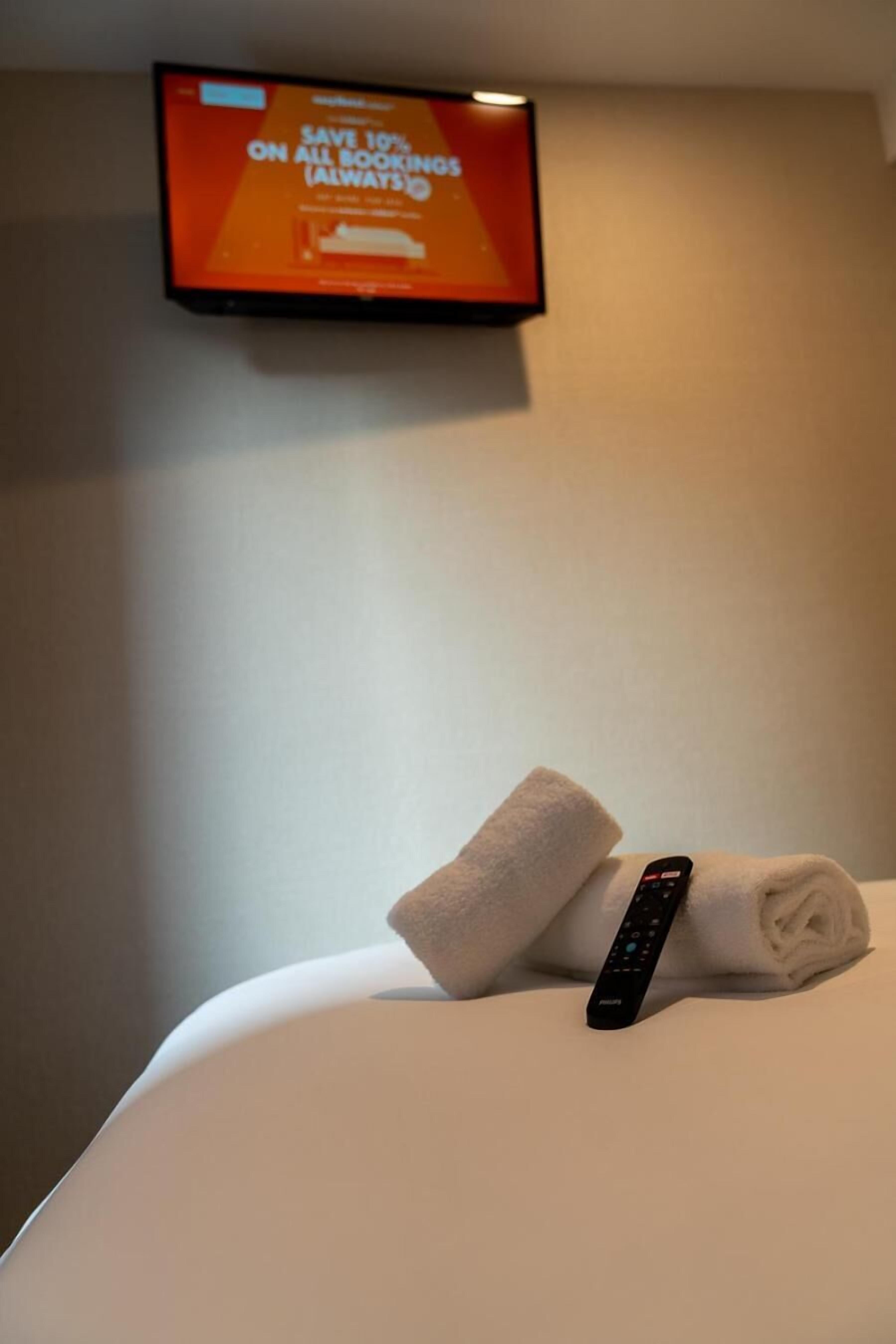 Habitación de hotel con cama, control remoto y televisor mostrando una oferta de reserva.