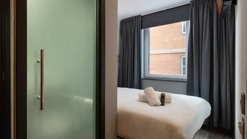 A compact hotel room with a bed, a window with curtains, and a door with a handle.