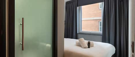 Ein kleines Hotelzimmer mit Bett, einem Fenster mit Vorhängen und einer Tür mit Griff.