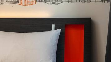 Une chambre d’hôtel avec un lit, une tête de lit ornée d’un panneau rouge et une fresque murale représentant un paysage urbain.