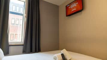 A hotel room with a bed, a remote control, and a TV displaying a promotional message.
