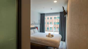 A hotel room with a large bed, a cityscape mural on the wall, and a view of a brick building outside.