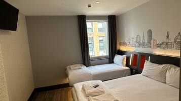Habitación de hotel con dos camas, un mural de paisaje urbano, una ventana con cortinas y un televisor de pantalla plana montado en la pared.