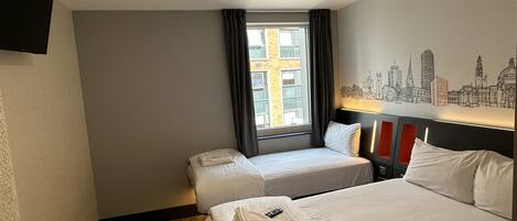 Une chambre d’hôtel avec deux lits, une fresque représentant un paysage urbain, une fenêtre avec des rideaux et un téléviseur à écran plat fixé au mur.
