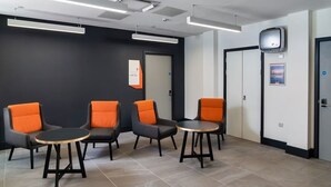 A waiting area with four chairs and two tables, a door, and a poster on the wall. - easyHotel Cardiff (Cardiff)
