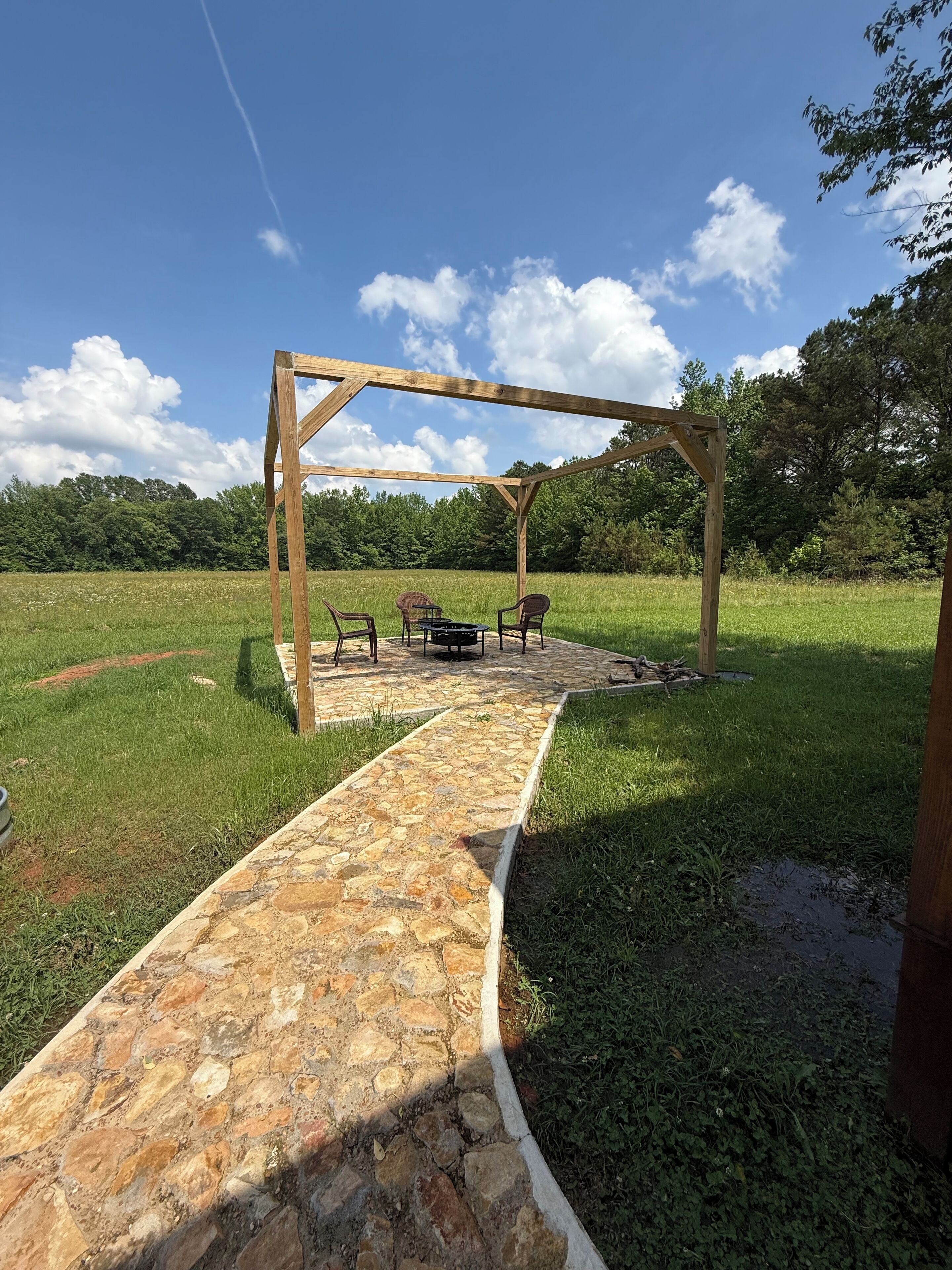 Een stenen pad dat leidt naar een houten pergola met een tafel en stoelen.