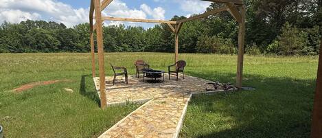 Een stenen pad dat leidt naar een houten pergola met een tafel en stoelen.