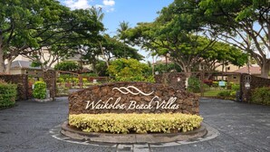 Un panneau indiquant l’emplacement de Waikoloa Beach Villas, avec une base en pierre et un parterre floral circulaire.