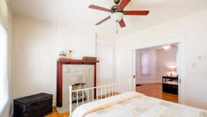 Une chambre à coucher avec un lit, un ventilateur de plafond, une commode en bois et une porte donnant sur une autre pièce.