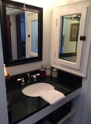 Une salle de bain avec un comptoir noir, un lavabo blanc et un grand miroir. On y trouve deux distributeurs de savon et une serviette accrochée au mur.