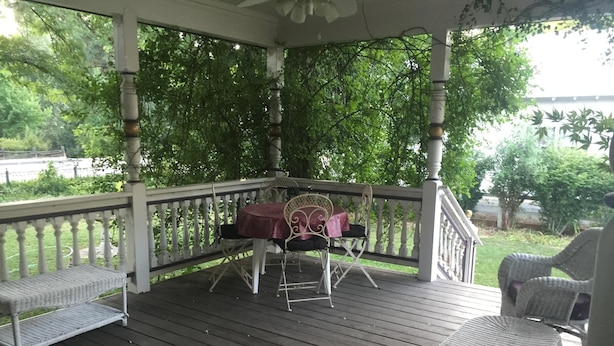 Une véranda avec une table et des chaises, entourée d’une terrasse en bois et de balustrades blanches.