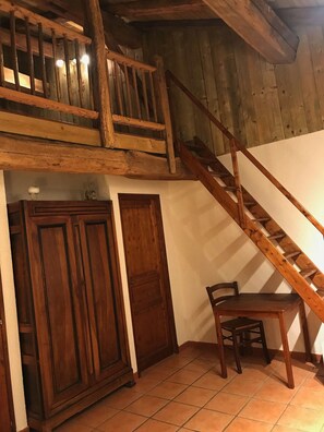Un escalier en bois, avec une chaise et un meuble, dans une pièce dont le sol est recouvert de carreaux.