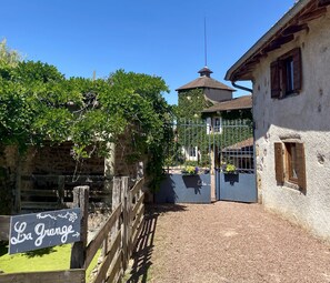 Un bâtiment rustique avec un mur en pierre, une clôture en bois et une enseigne indiquant « La Grange ».