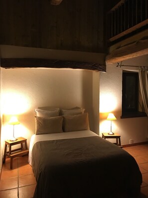 Une chambre à coucher faiblement éclairée, avec un lit, deux lampes de chevet et une fenêtre avec des rideaux.