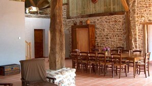 A rustic dining area with stone walls, wooden furniture, and a high ceiling. - La Grange : La Chambre Vendange (Coutouvre)