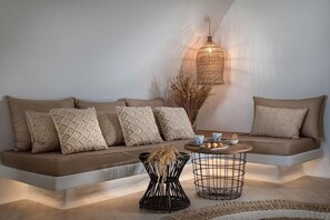 A modern living room with a sofa, a round coffee table, and a hanging light fixture. - White (Santorini)
