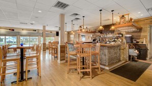 Un restaurante con mesas y sillas de madera, una zona de bar con mostrador de piedra y lámparas colgantes.