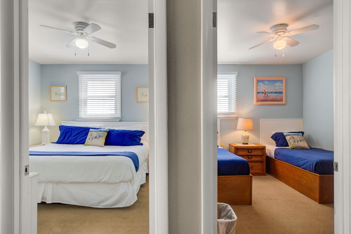 A bedroom with a bed, bedside tables, a lamp, a ceiling fan, and a window with blinds.